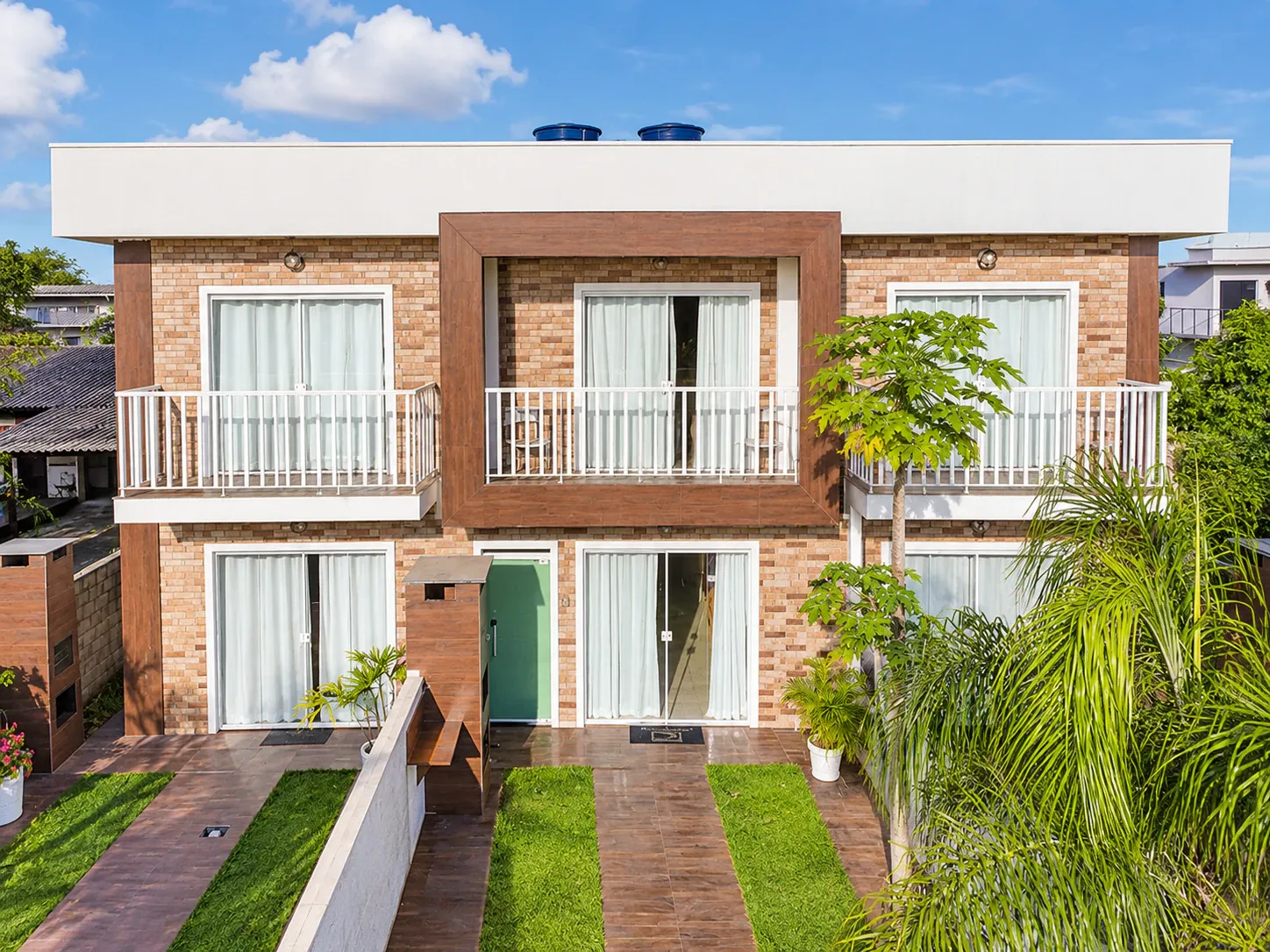 Fachada de dois pavimentos da Moradas do Campeche, com tijolos aparentes, varandas e jardim
