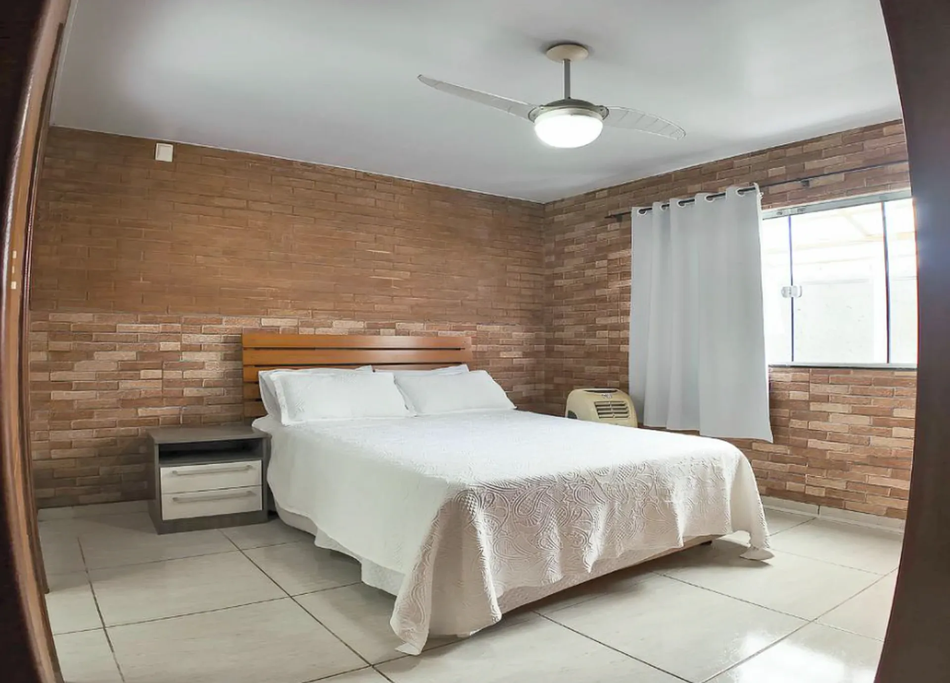 Quarto com cama de casal, paredes de tijolos aparentes e ventilador de teto