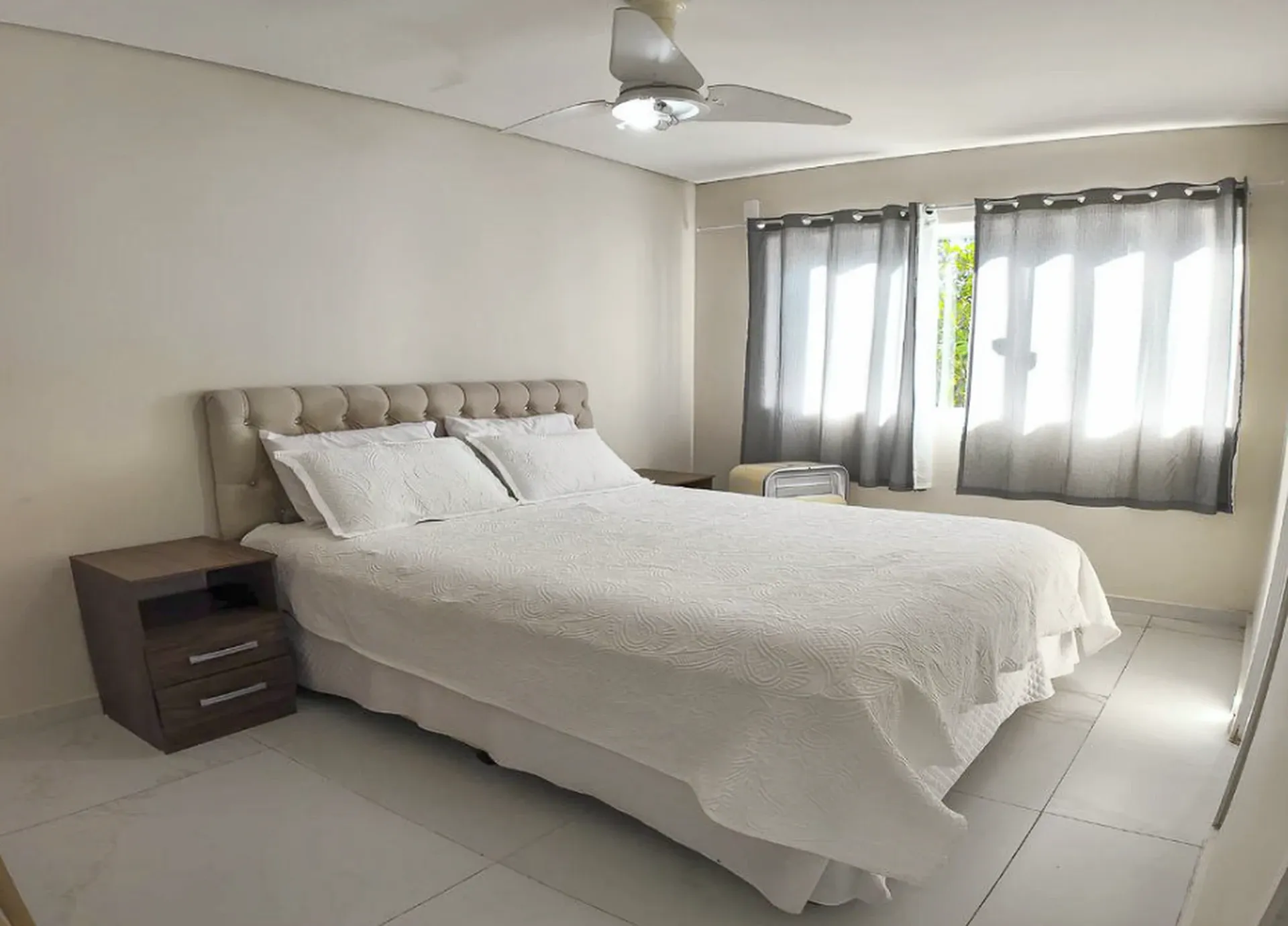 Quarto claro com cama de casal, mesas laterais e janela com cortinas